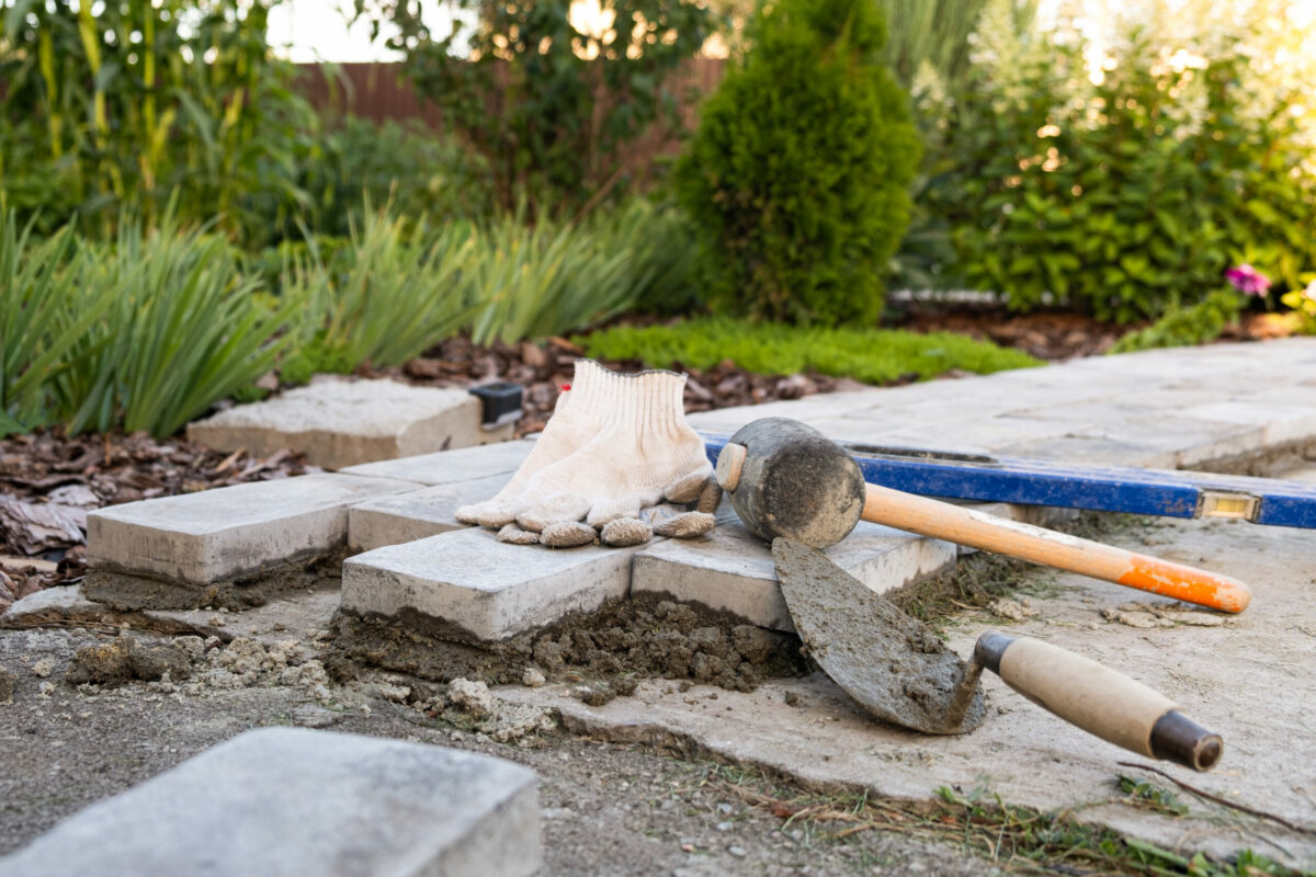 Handschuhe, Pflastersteine, Werkzeug, frischer Zement.